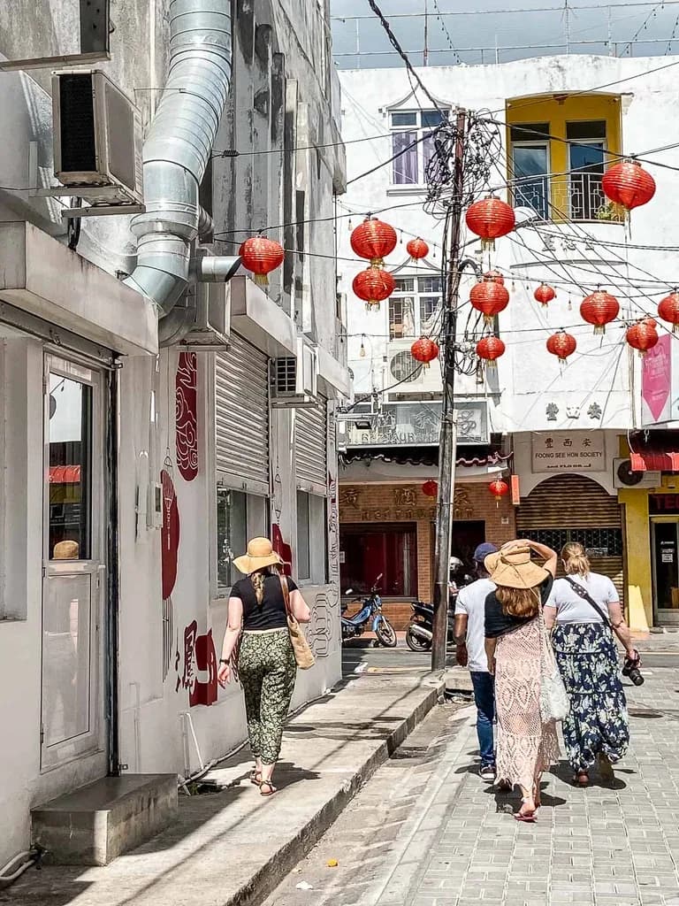 Pedestrians beneath red lanterns in a narrow Chinatown street in Port Louis