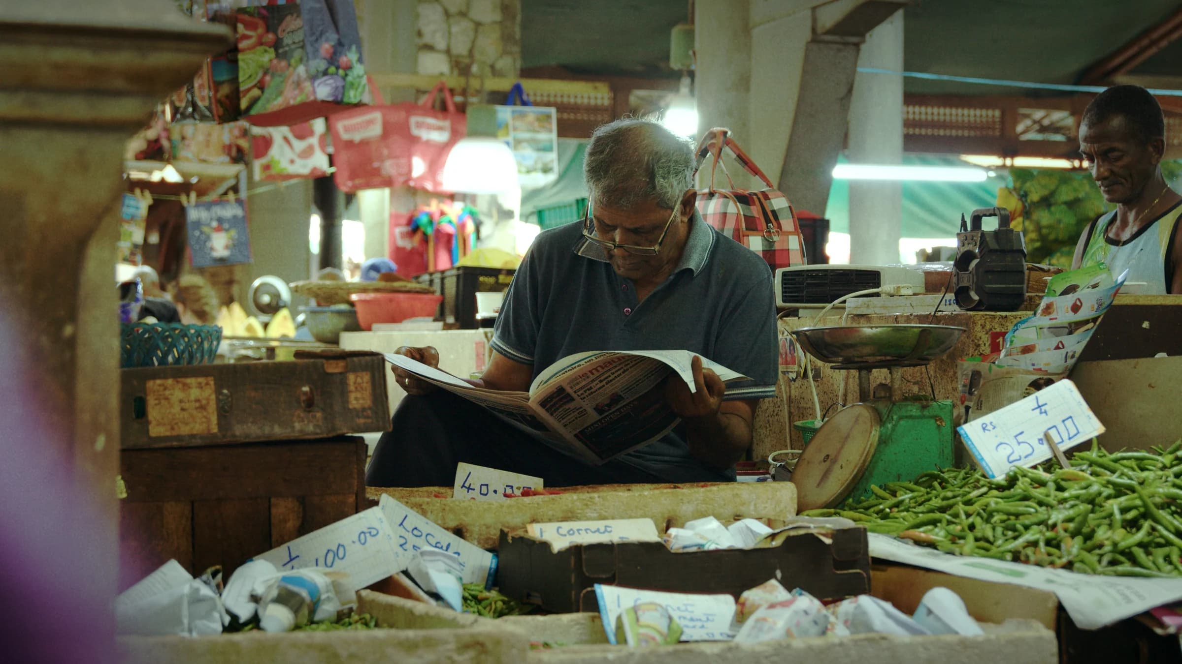 A market vendor reads a newspaper among his produce
